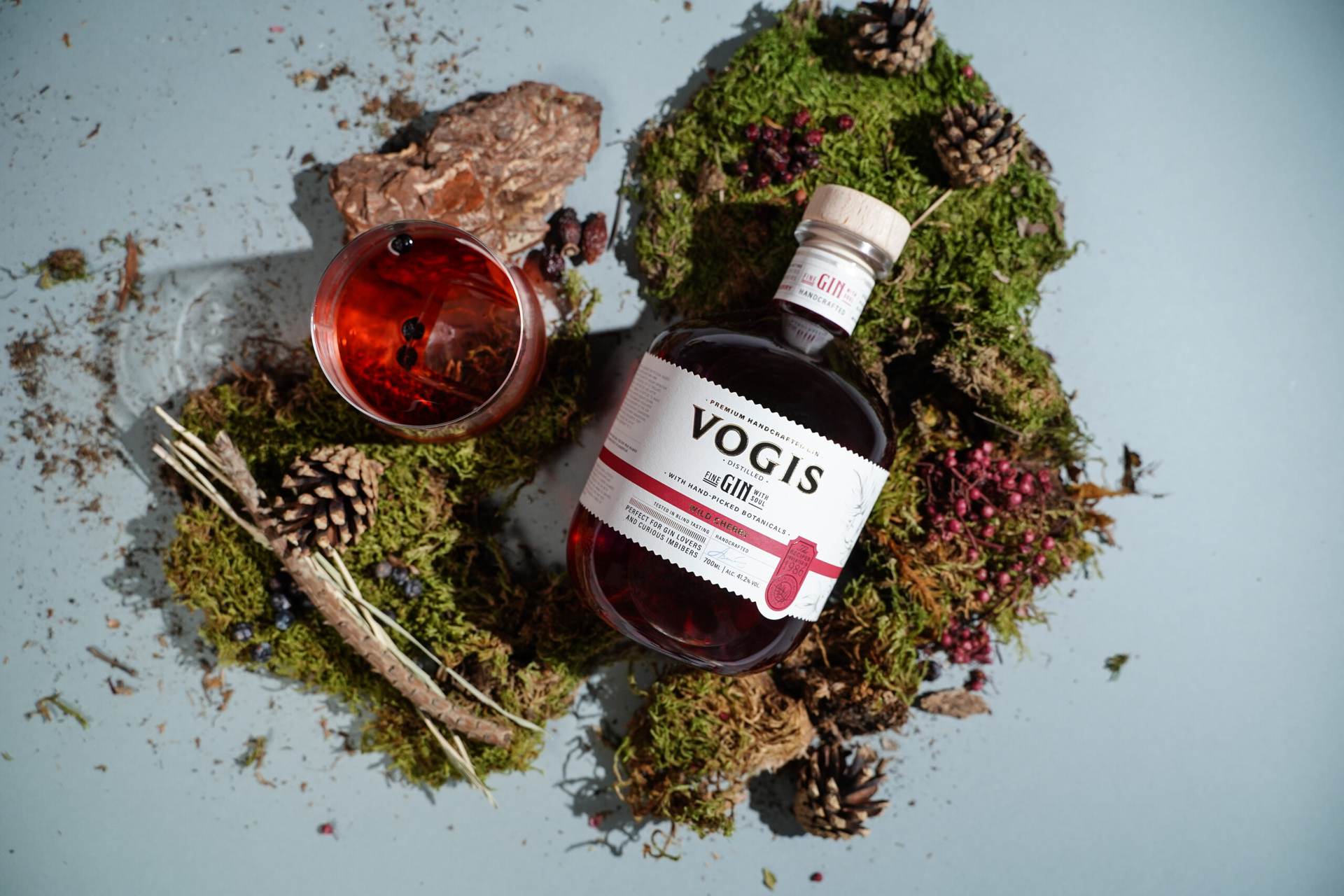 Vogis Wild Cherry Gin bottle with a cocktail glass surrounded by moss and botanicals